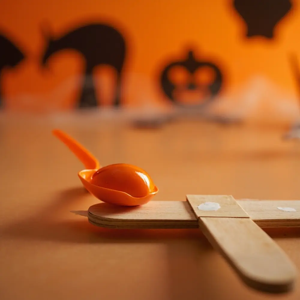 How to Engineer a Halloween Candy Catapult with Popsicle Sticks 4 Stick popsicle spoon hot the plastic up focusing catapult secure a close end on h3 to of carefully onto hand image shot 4 applying arm detailed glue