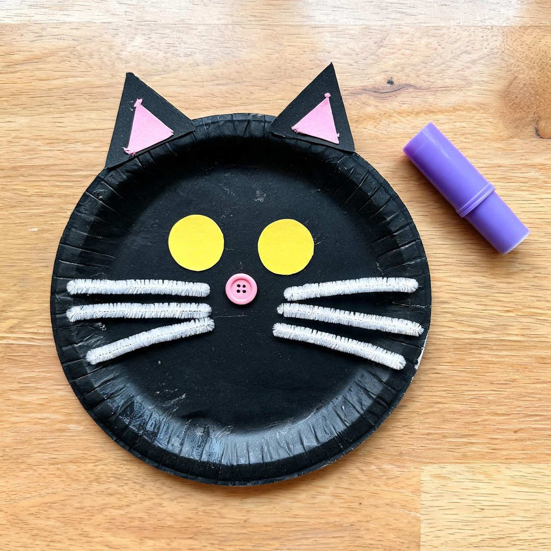 Paper Plate Whisker Black Cat - Black painted paper plate cat face with pink inner ears and white pipe cleaner whiskers