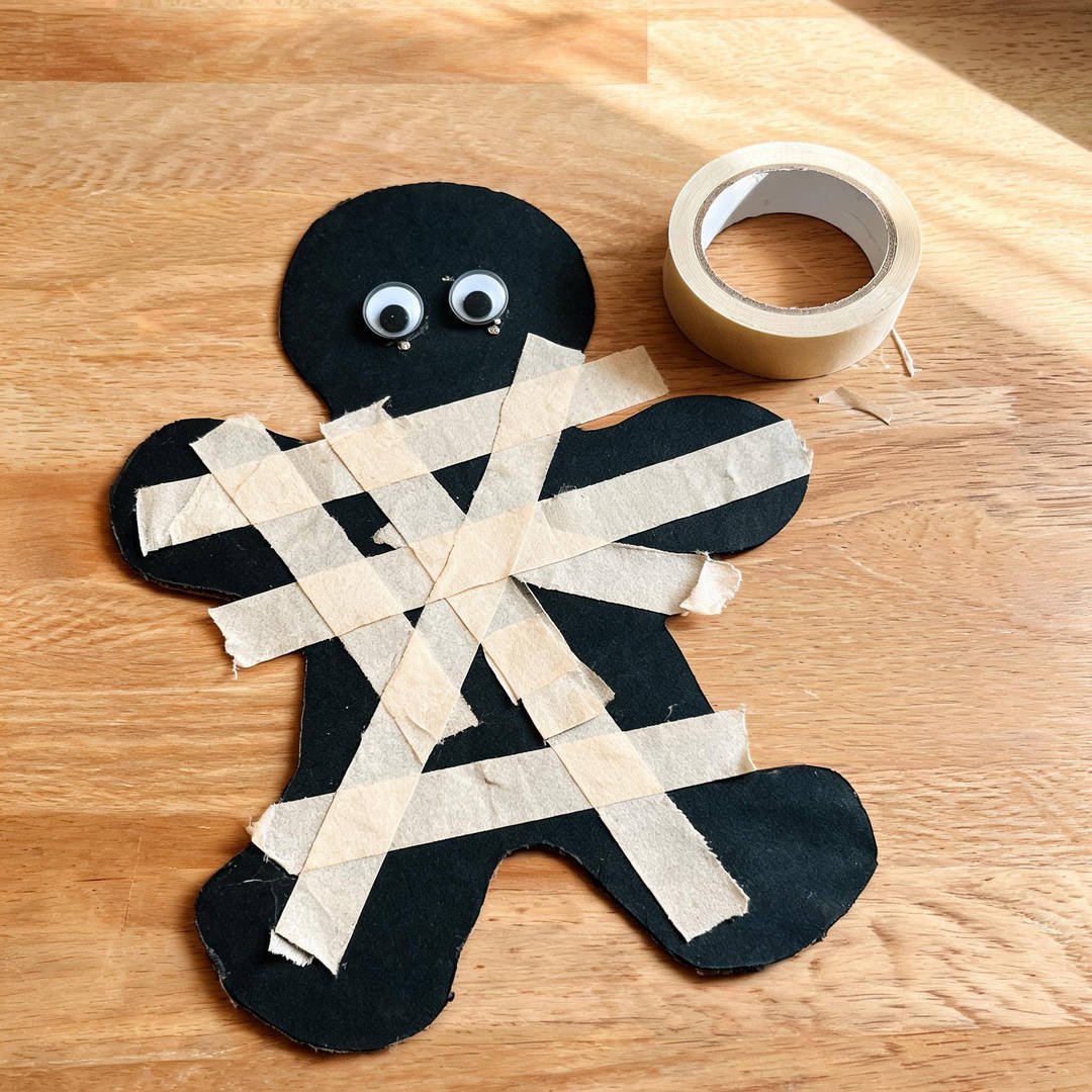 Masking Tape Resist Mummy - Flat black cardstock mummy cutout wrapped in torn strips of cream masking tape